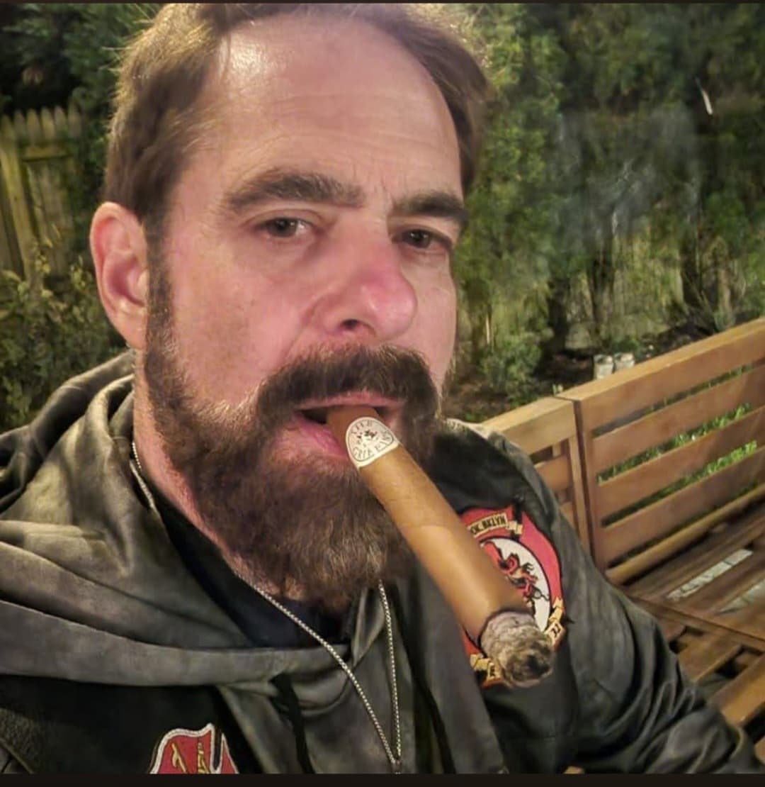 Cinematic low-key portrait of a distinguished man enjoying a premium cigar, wisps of smoke swirling in dark atmospheric lighting