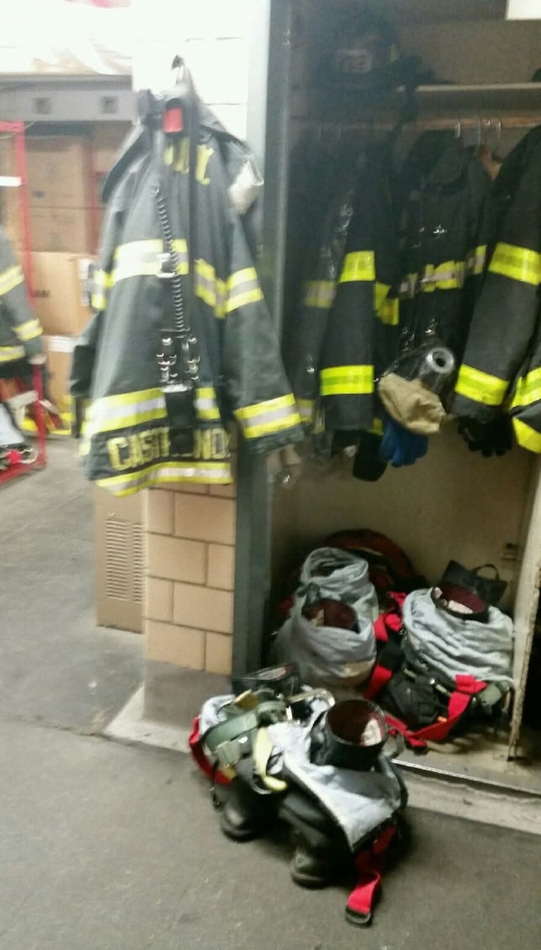 Close-up of weathered firefighter turnout gear and helmet in a dark industrial locker room
